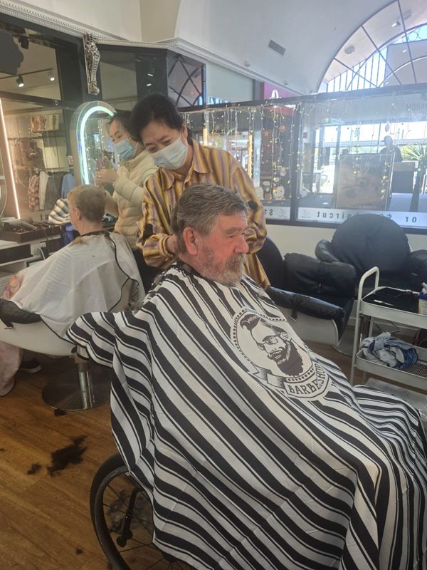 A participant having a haircut at the local barber with support nearby